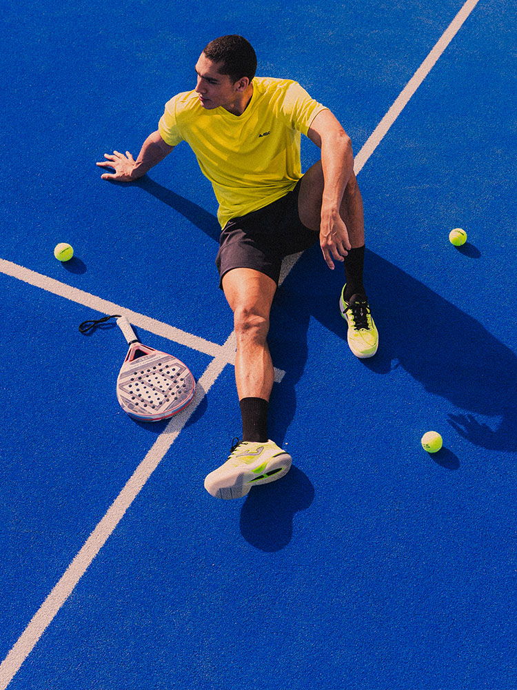 Ragazzo che seduto su campo da padel vestito con apparel tecnico, racchetta padel e palline